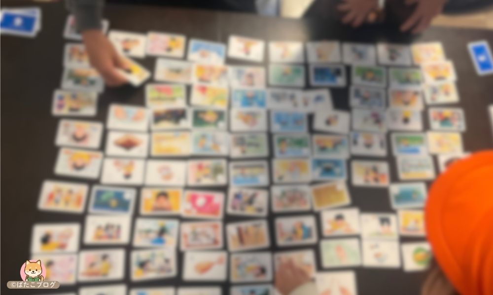 大ピンチずかんカルタを家族で遊んでいる様子。100枚を広げた圧巻の場面（ぼかし加工）